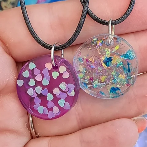 Due ciondoli in resina con piccoli cuori chiari e inclusioni colorate su una mano